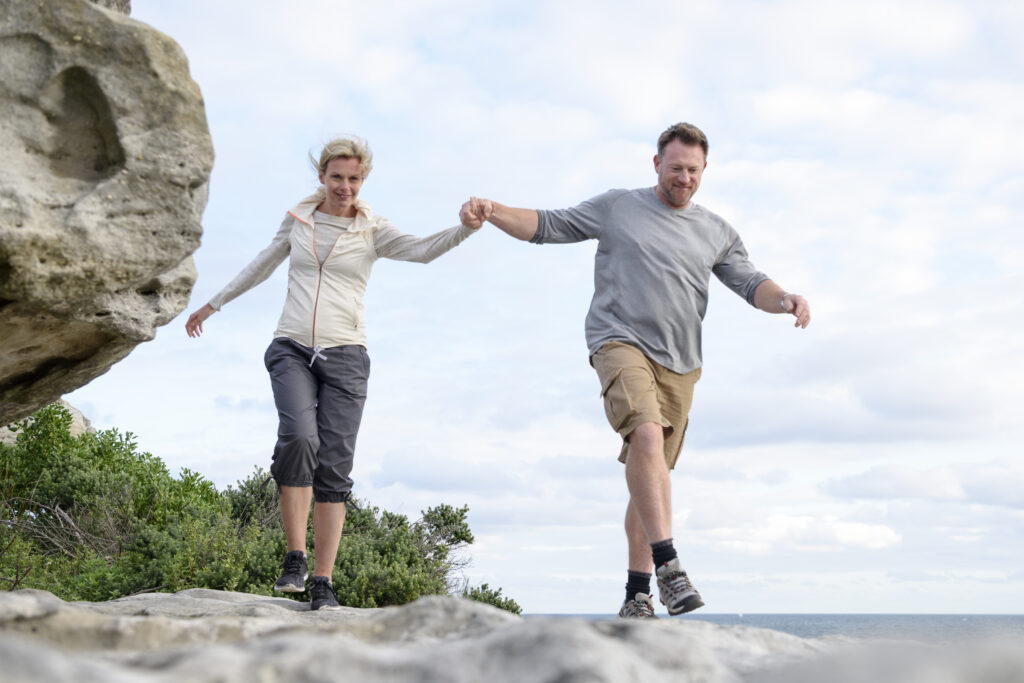 Mature Couple Hiking On Rocks Holding Hands, Bondi Beach